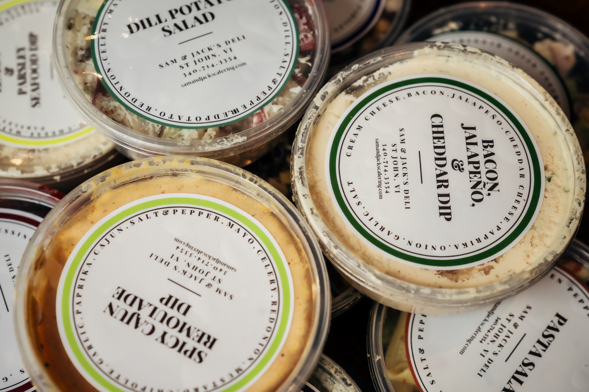 Close-up of Sam & Jack's labeled deli containers: dill potato salad, bacon jalapeño cheddar dip, spicy cajun remoulade.